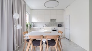 A modern kitchen with white cabinets, a central island, and a dining area with a table and chairs. - Warta River Comfort Apartment (Poznań)