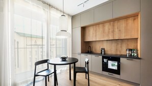 A modern kitchen with a round dining table, two chairs, wooden cabinets, and a view of buildings through large windows. - Centrum Nauki Kopernika Luxury Studio (Warszawa)
