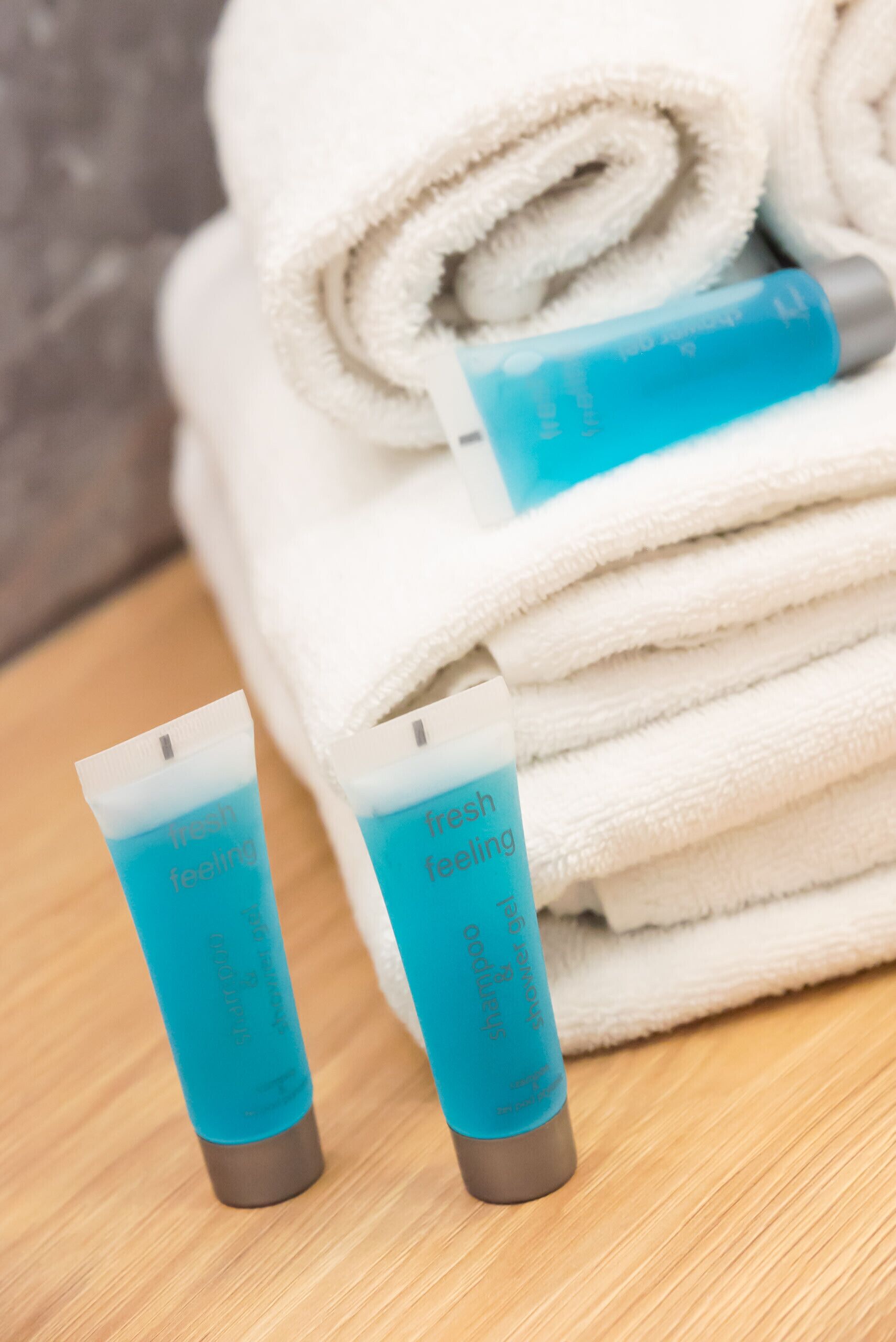 A stack of white towels and two tubes of 'fresh feeling' body wash on a wooden surface.