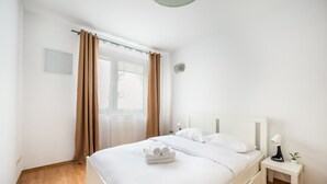 A neatly made bed with white linens and a small bedside table with a lamp and a plant. - KEN 54 2-Bedroom Apartment (Warszawa)