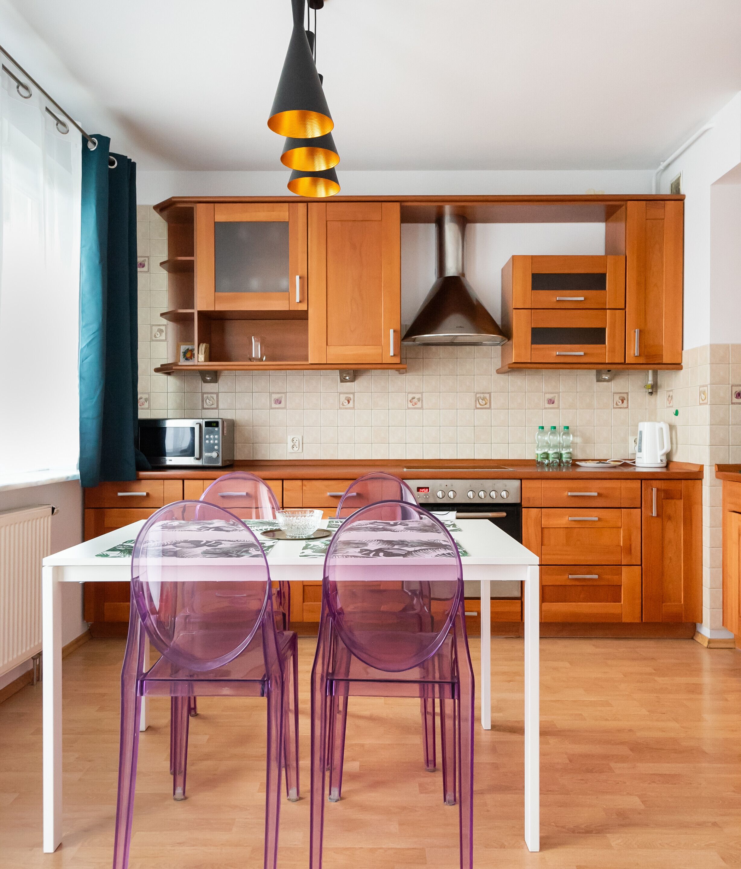 A modern kitchen with wooden cabinets, a white countertop, and a dining table with transparent chairs.