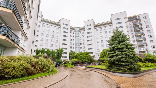 A multi-story residential building with a curved driveway, surrounded by greenery and parked bicycles. - KEN 54 2-Bedroom Apartment (Warszawa)