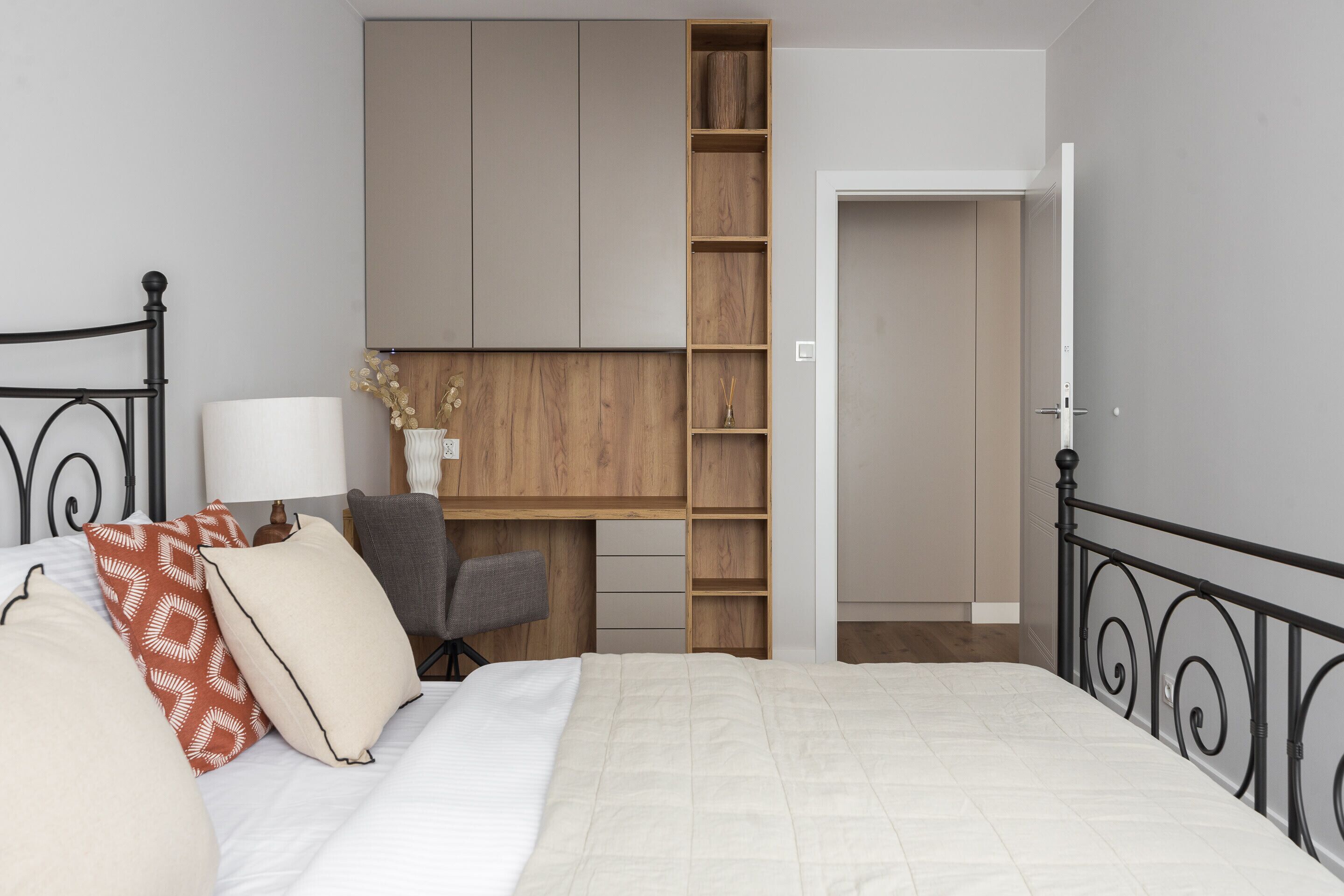 Quarto com cama, mesa de cabeceira, luminária, cadeira e estante de madeira embutida.