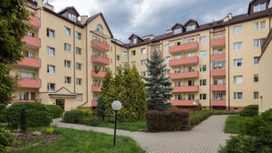 A multi-story residential building with balconies, a paved pathway, and surrounding greenery.