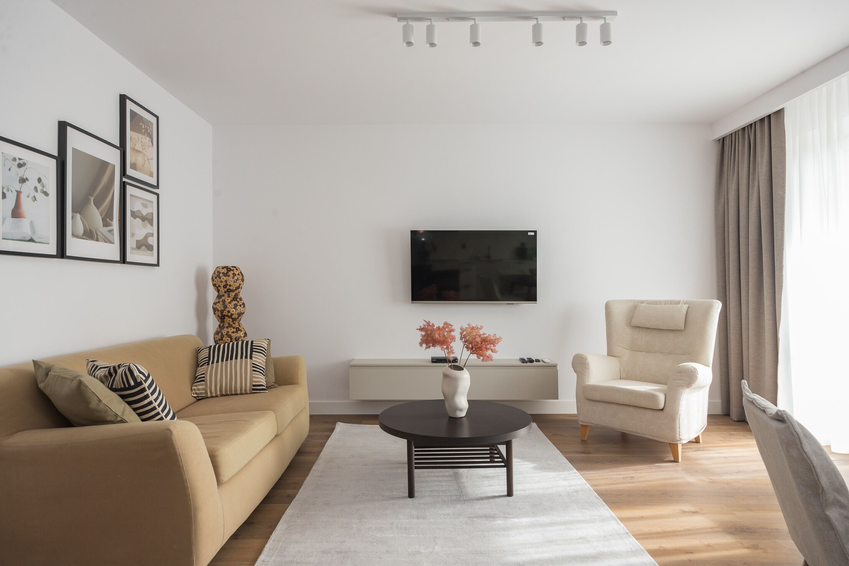 Ein modernes Wohnzimmer mit einer Couch, einem Sessel, einem Couchtisch und einem an der Wand befestigten Flachbildfernseher.