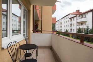 Un balcon avec deux chaises et une table, donnant sur un quartier résidentiel avec des bâtiments blancs et un toit rouge.