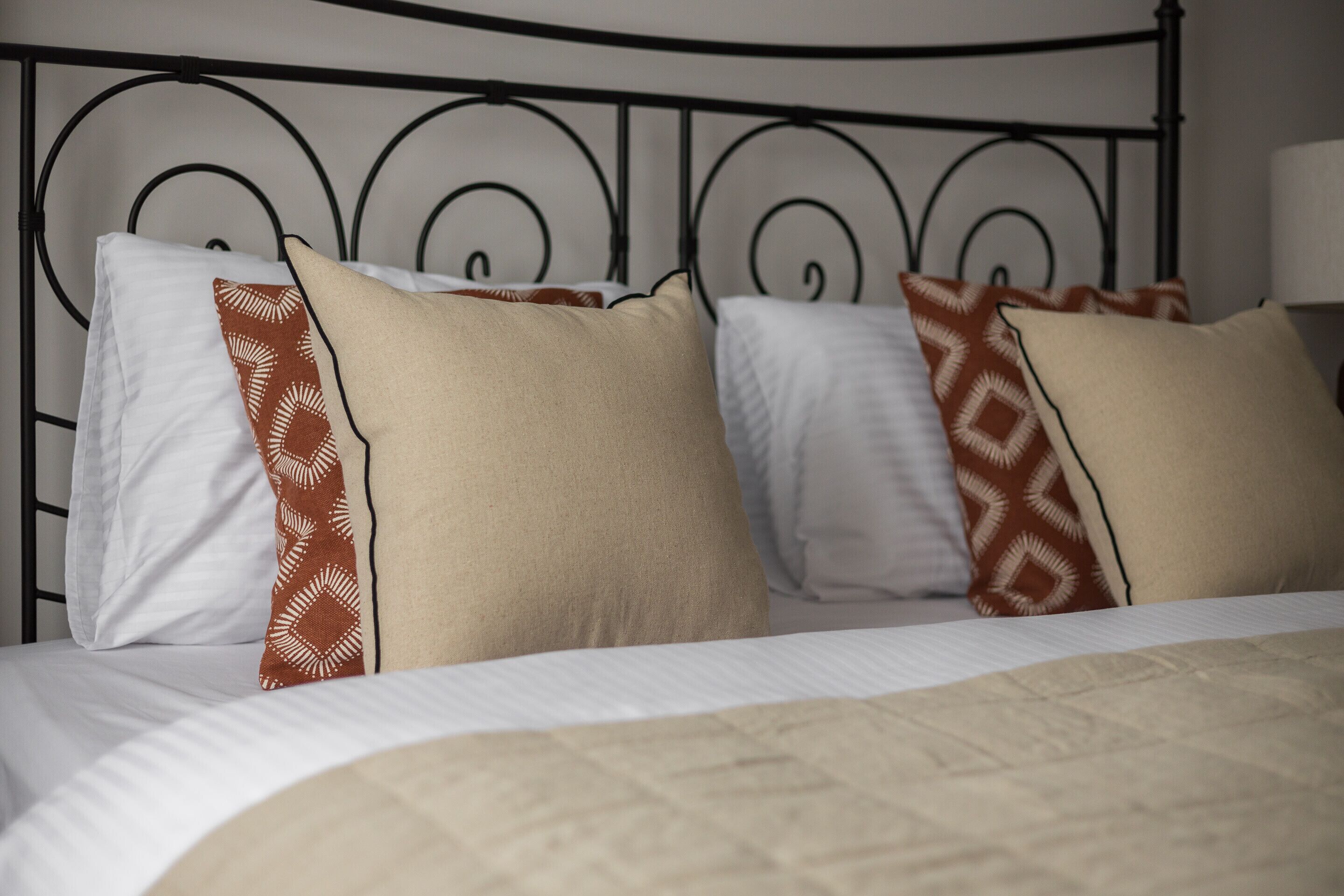 Una cama con una colcha estampada y varios almohadones, incluyendo un almohadón blanco y dos con un diseño geométrico.
