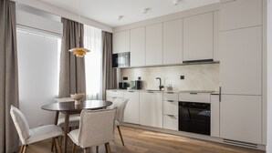 A modern kitchen with white cabinets, a built-in oven, and a dining area with a round table and four chairs.