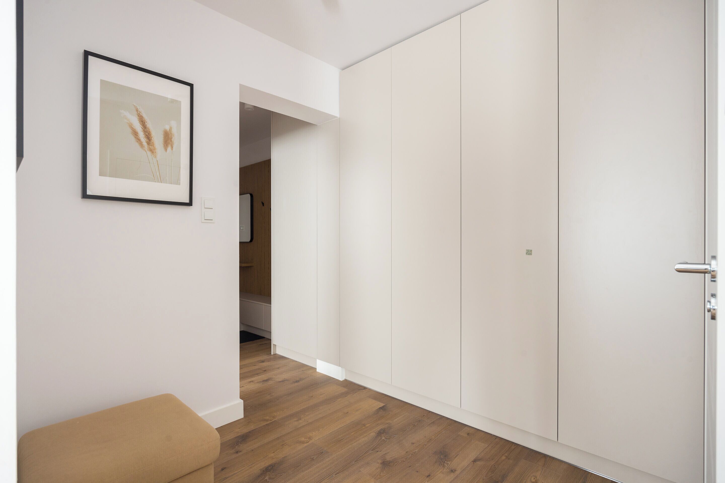 A hallway with a framed picture, a bench, and a wardrobe.
