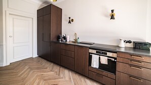 A modern kitchen with dark wood cabinets, a stainless steel sink, and a built-in oven. There are two pendant lights above the counter and a small wall-mounted light.
