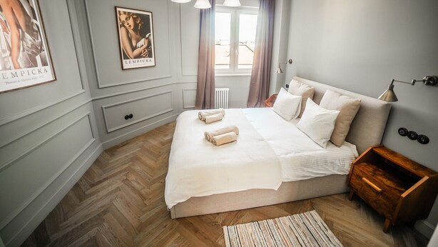 A bedroom with a large bed, a wooden nightstand, a framed portrait, and a window with curtains.