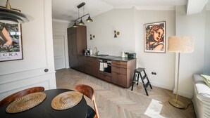 A modern kitchen with wooden cabinets, a central island, and pendant lighting. There is a dining area with a table and chairs, and a floor lamp.