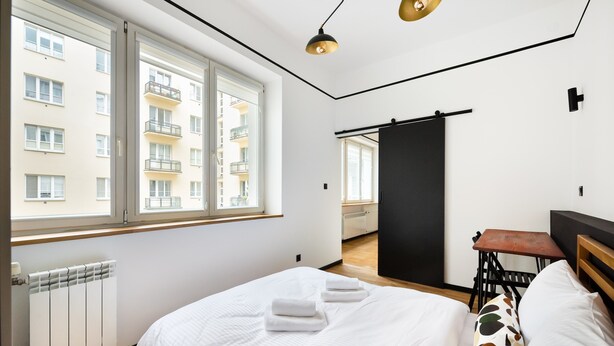 Ein modernes Hotelzimmer mit einem großen Bett, einem kleinen Tisch und Blick auf die Stadt durch große Fenster.