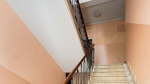 Eine Treppe mit hölzernem Geländer und schwarzen Metallspindeln, die zu einer Zwischenebene mit weißer Decke und beigen Wänden führt.