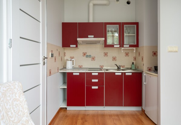 A compact kitchen with red cabinets, a white countertop, and a built-in oven.