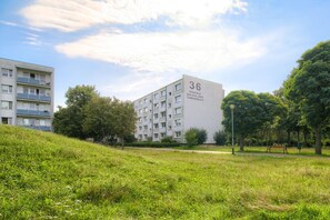 Ein mehrstöckiges Wohngebäude mit Balkonen, einer Rasenfläche mit einer Bank und Bäumen.