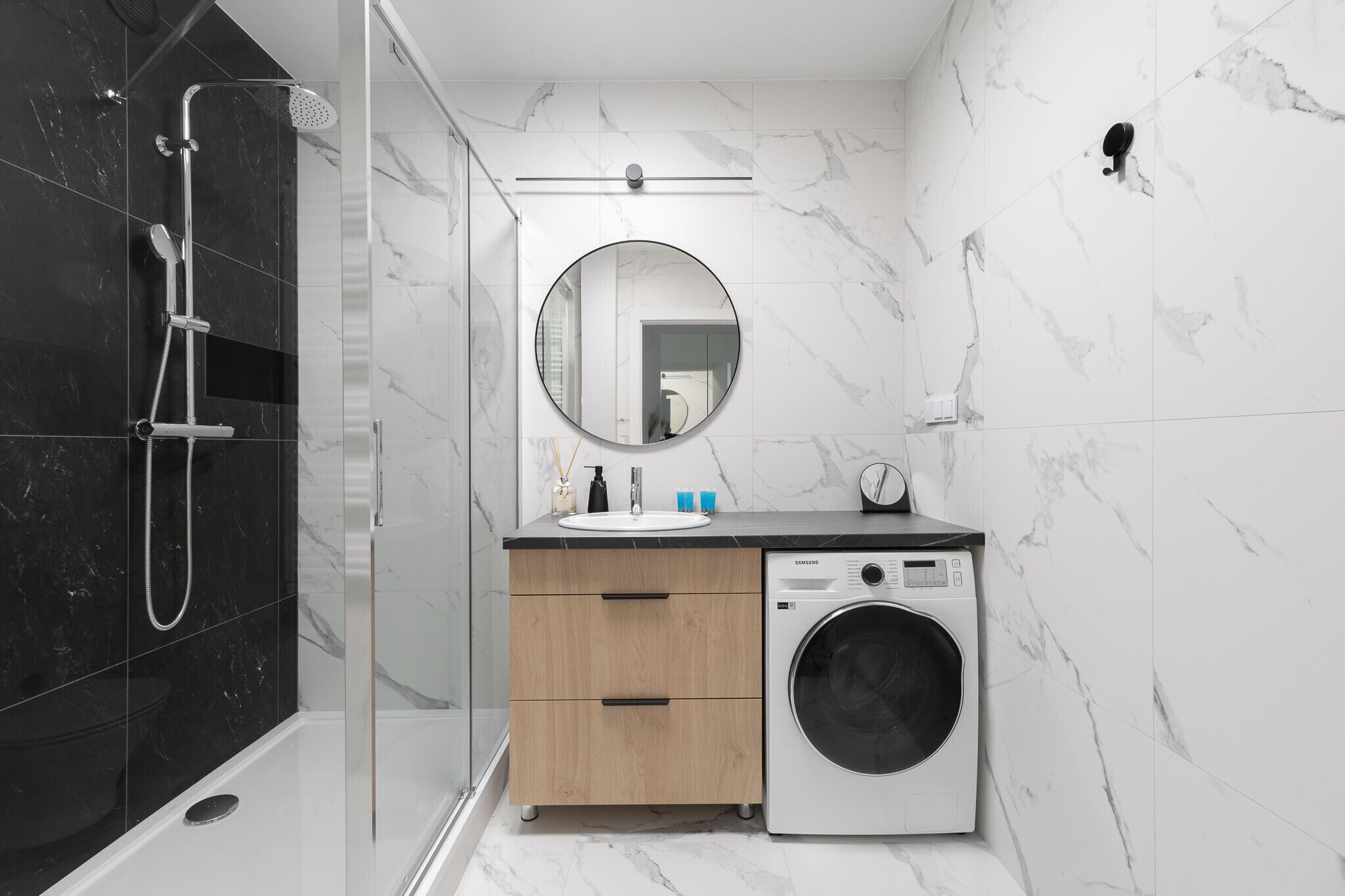 Een moderne badkamer met een douchecabine, een ingebouwde wasmachine en een houten wastafelmeubel met spiegel.