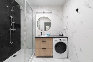Ein modernes Badezimmer mit einer Glaskabine für die Dusche, einer integrierten Waschmaschine und einem Holzbadezimmer-Möbel mit Spiegel.