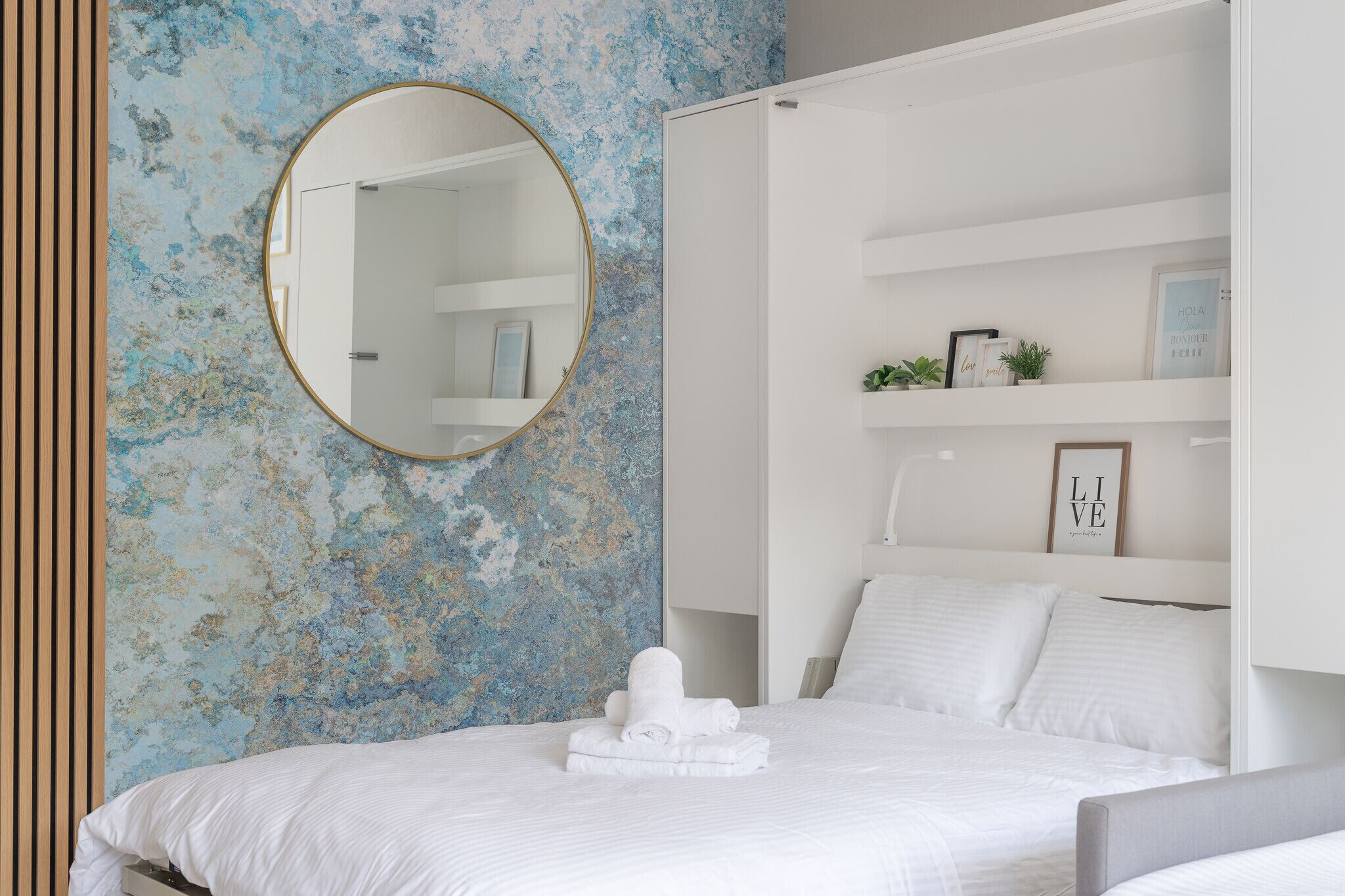 A bedroom with a bed, a round mirror, and a wall with a blue and white abstract pattern.