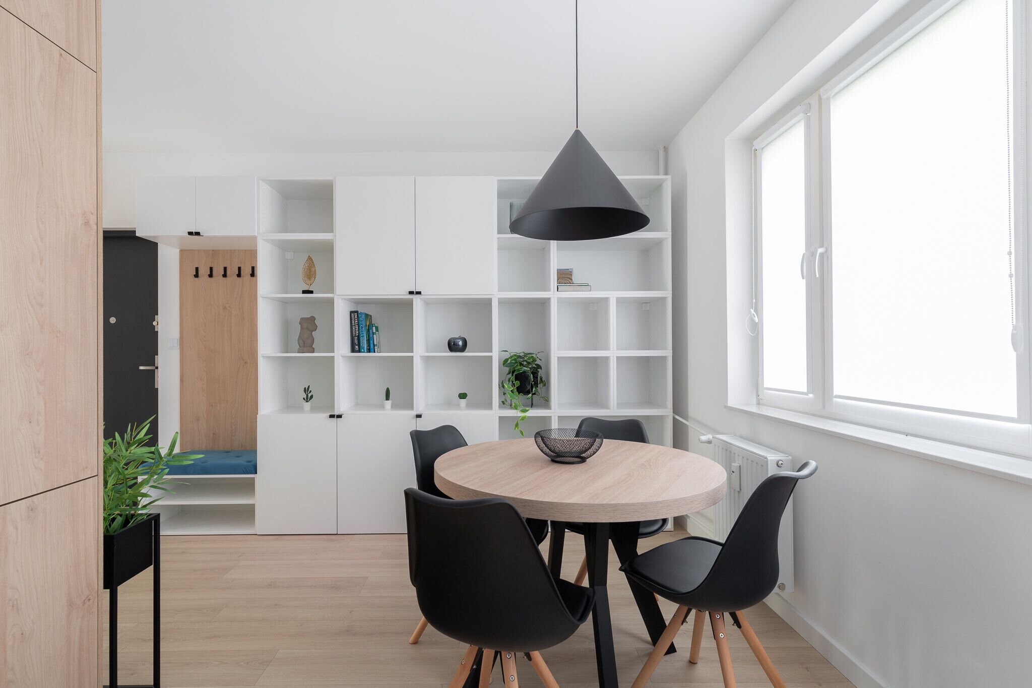 Uma sala de jantar moderna com uma mesa redonda, cadeiras pretas, uma luminária pendente preta e estantes brancas.