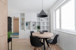 Ein moderner Essbereich mit einem runden Tisch, schwarzen Stühlen, einer schwarzen Pendelleuchte und weißen Regalelementen.