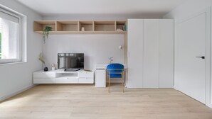 Een moderne, minimalistisch ingerichte kamer met een wit bureau, een blauwe stoel, een televisie en ingebouwde planken.