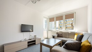 A modern living room with a flat-screen TV, a wooden coffee table, a grey sofa with cushions, and a large window with blinds. - Rondo ONZ City View Apartment (Warszawa)