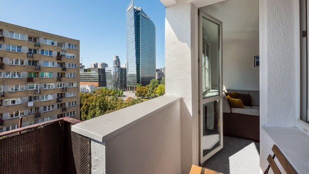 A balcony with a view of a modern high-rise building, a wicker chair, and a sofa with cushions. - Rondo ONZ City View Apartment (Warszawa)