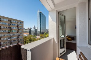 A balcony with a view of a modern high-rise building, a wicker chair, and a sofa with cushions. - Rondo ONZ City View Apartment (Warszawa)