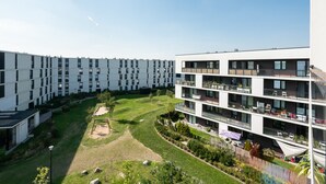 Un immeuble d’appartements moderne, doté de plusieurs étages, de balcons et d’une cour intérieure avec pelouse et plantes.