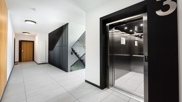 Un couloir moderne avec un escalier, un ascenseur et une porte portant le numéro 3.