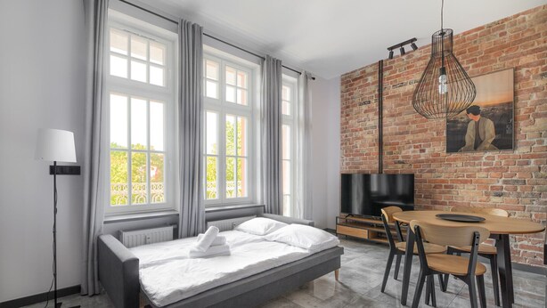 A modern bedroom with a large bed, a dining table, and a brick wall.