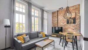 A modern living room with a grey sofa, a wooden coffee table, and a dining area with a brick wall and a hanging light fixture.