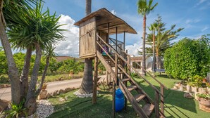 Ein hölzernes Baumhaus mit Treppe, umgeben von Palmen und Grünpflanzen.