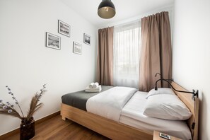 Une chambre à coucher bien rangée, avec un lit en bois, une table de chevet, une télécommande et un vase contenant des fleurs séchées.