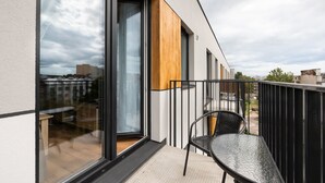 Een modern balkon met een glazen deur, een metalen hekwerk en een tafel met stoelen.