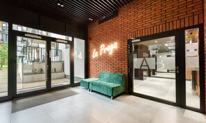 Un intérieur moderne avec une enseigne au néon indiquant « La Praga », un canapé vert et une porte en verre donnant sur l’extérieur.