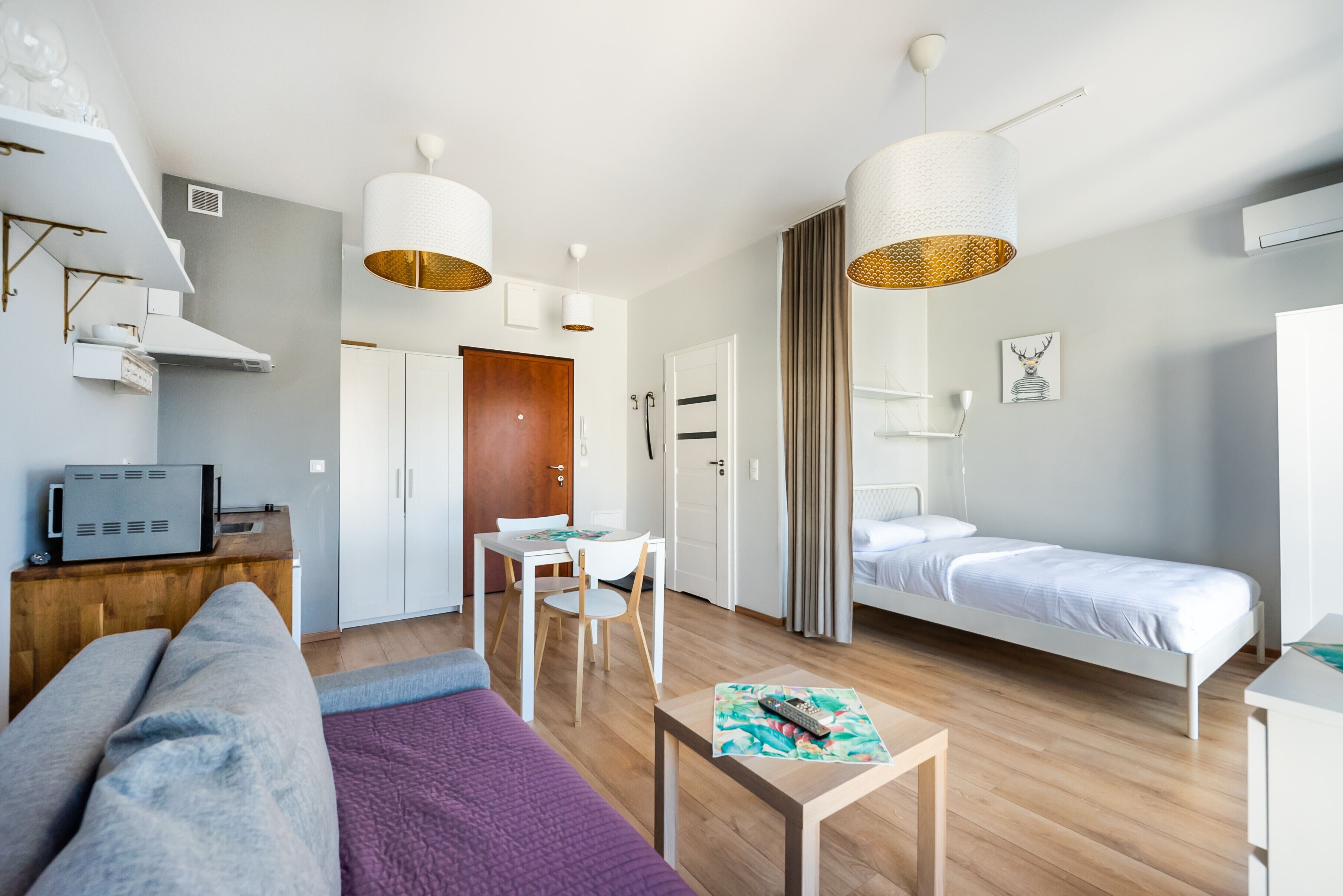 A modern, well-lit room with a bed, a sofa, a small dining table, and a TV.