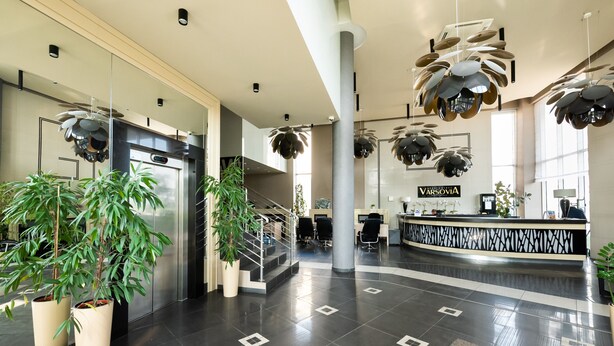 Un hall d’entrée moderne avec un comptoir d’accueil, des plantes en pot et un escalier.