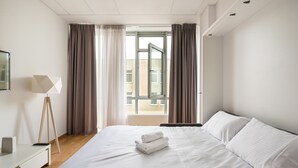 Une chambre d’hôtel avec un grand lit, un bureau avec une lampe et une vue sur l’extérieur par une fenêtre.