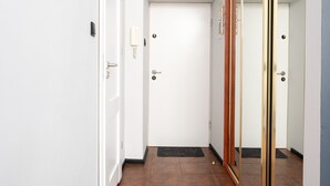 Un couloir avec une porte blanche, un téléphone et un miroir doté d’un cadre doré.
