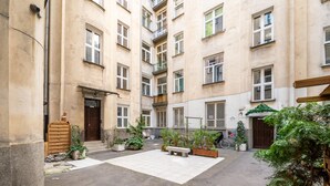 Une cour avec une zone pavée, des bancs, des plantes en pot et une porte en bois.