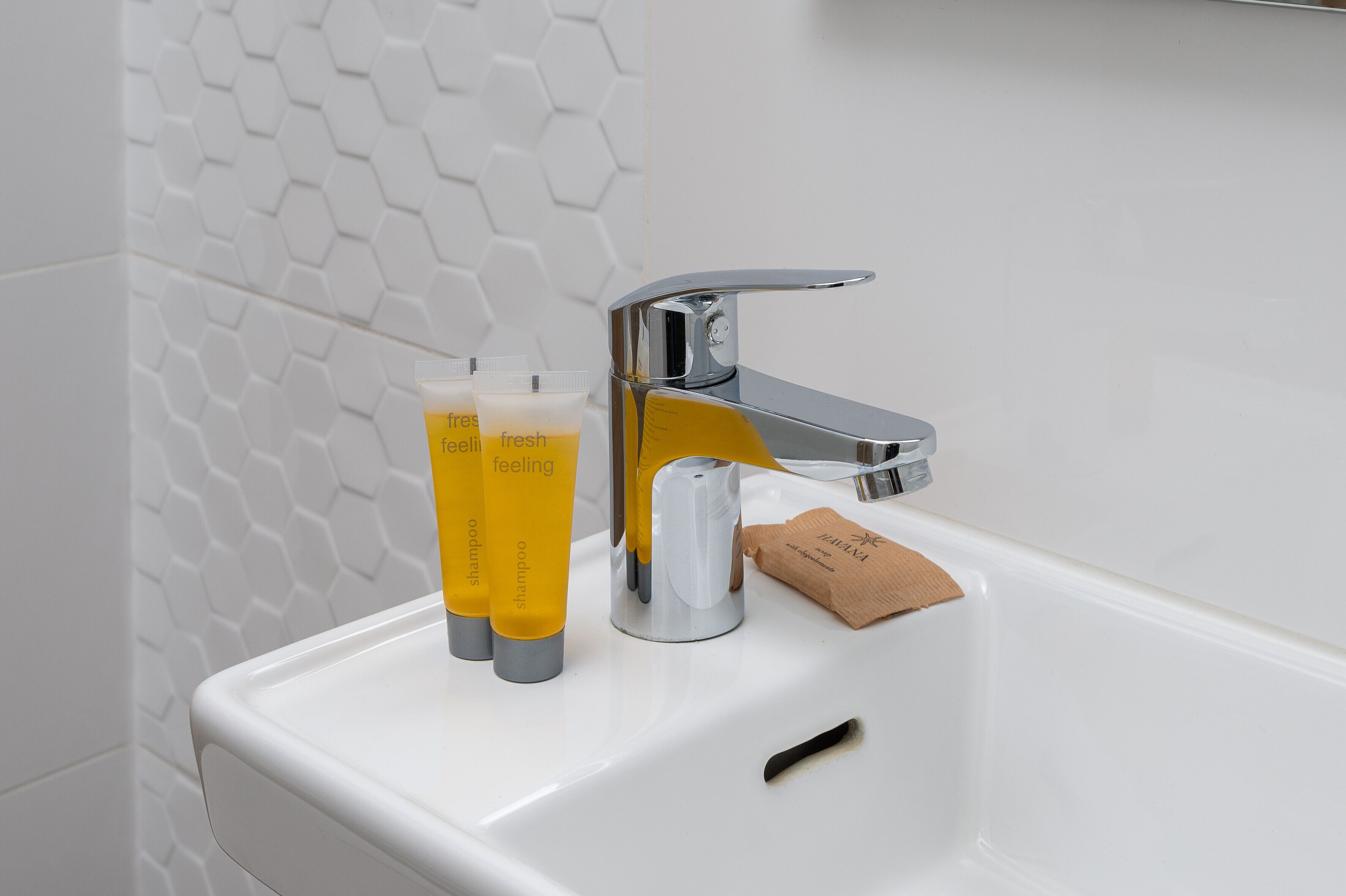 A bathroom sink with a chrome faucet, two yellow shampoo bottles, and a bar of soap.