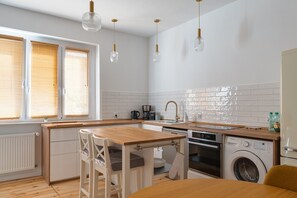 Una cocina moderna con encimeras de madera, horno integrado, lavadora y comedor con mesa y sillas de madera.