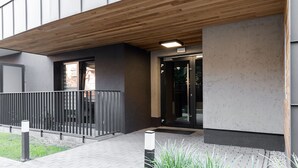 Una entrada moderna a un edificio con techo de madera, una cerca de metal negro y un camino pavimentado que conduce a la puerta.