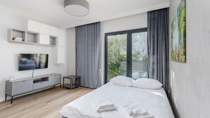 Un dormitorio moderno con cama, televisor, consola y balcón con cortinas.