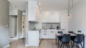Una cocina moderna con armarios blancos, una mesa de comedor de madera con sillas negras y una lámpara colgante.