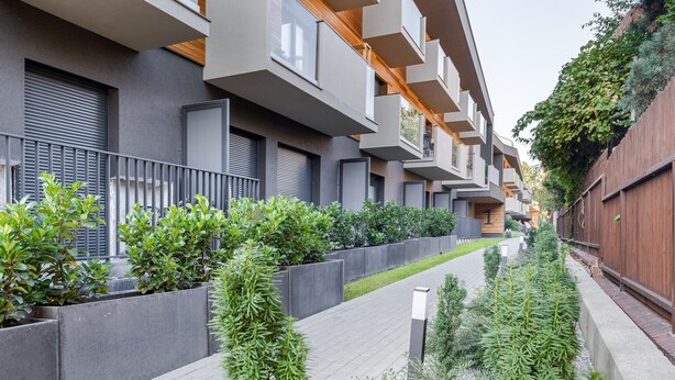 Un moderno edificio de apartamentos con balcones, un paseo empedrado y vegetación.