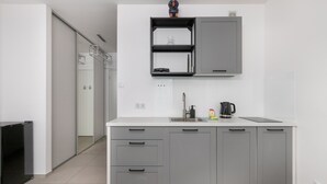 Une cuisine moderne avec des meubles gris, un plan de travail blanc et une étagère intégrée au-dessus de l’évier.