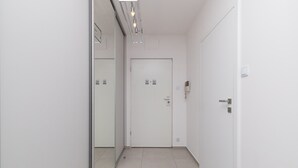 Un couloir étroit aux murs blancs et au sol carrelé, qui mène à une porte dotée d’un trou de serrure et d’un téléphone fixé au mur.